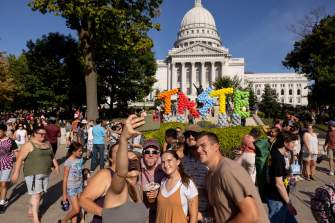 A group of six white adult men and women take a selfie in front of a balloon installation that says TASTE at the Wisconsin State Capitol during Taste of Madison