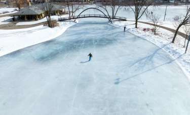 An aerial shot of a person ice skating on a frozen Tenney Park lagoon