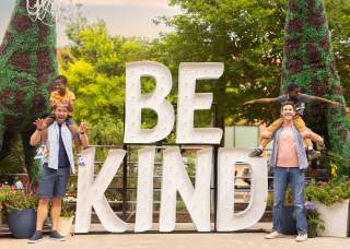 Family laughing in front of Be Kind sign at Elsewhere Garden Bar & Kitchen