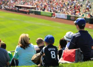 Kid sitting in a crowd at a baseball game with jersey and glove on.