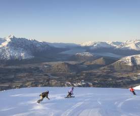 Three snowboarders riding down snowy mountain