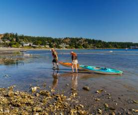 Two people pulling their kayaks out of the water and onto the beach