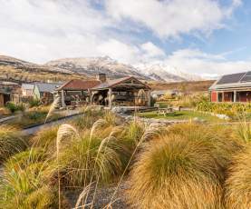 Exterior view of The Headwaters Eco Lodge, with native bush, rustic cabins and snowy mountains in the background