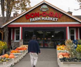 Shopper walking into Don-O-Ray Farm Market in Kelowna between outdoor displays of farm-grown pumpkins and squash.
