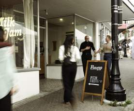 A welcoming moment outside a Nanaimo café and pizza shop, with people chatting and walking along a busy downtown sidewalk.