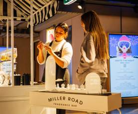 A white stand inside a shop with two girls making perfume