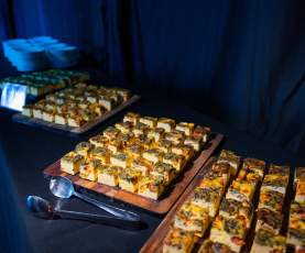 A catering table set up in a dark event room with square quiche's on wooden serving boards