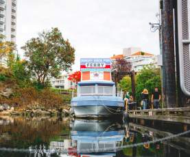 A small ferry at a dock labelled ‘Dinghy Dock Pub Ferry,’ with people boarding and reflections in the calm water.