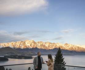 People enoying a wine on the balcony of Nest Kitchen and Bar overlooking the snow-covered Remarkables mountain range