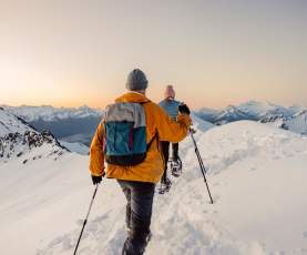 Point of view image with two people snow shoeing surrounded by snow covered mountains