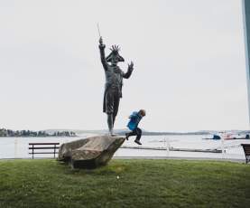 A kid jumping from a rock with a statue onto the grass.