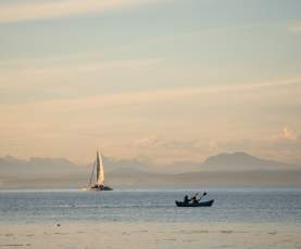 A kayak and sailboat on the ocean as the sun begins to set with mountains in the distance