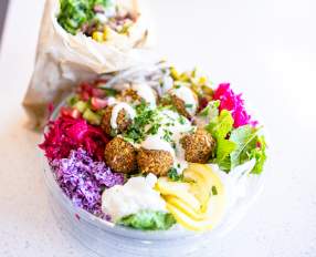 Falafel bowl with fresh vegetables, pickled cabbage, hummus and creamy sauce beside a wrapped sandwich