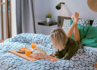 Woman-laying-down-on-hotel-bed-having-breakfast
