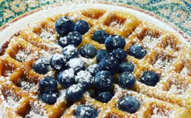A waffle on a patterned plate topped with blueberries and powdered sugar.