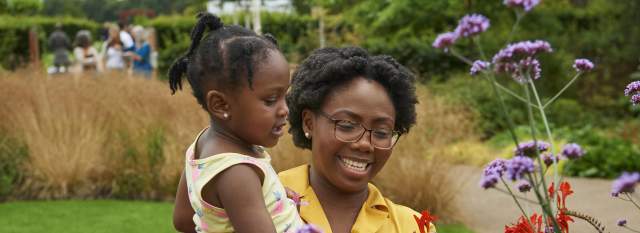 A woman holding a child looking at plants