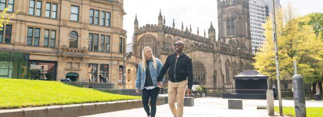Couple walking outside Manchester Cathedral and Corn Exchange.