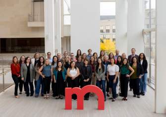 The entire Destination Madison team of about 35 people stand in a group at the Overture Center with a large red m statue in front of them