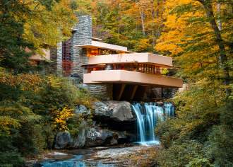 Iconic architectural building Fallingwater sits atop a waterfall with fall foliage surrounding.