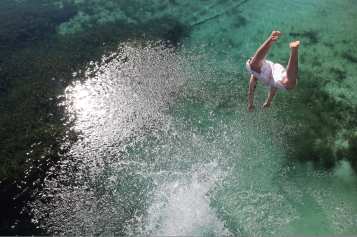 An airborne diver caught in flight before plunging into a natural spring.