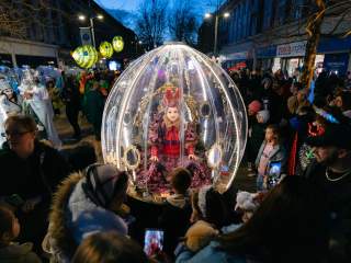A show globe, a giant showglobe with a artist inside is surrounded by people watching the procession.