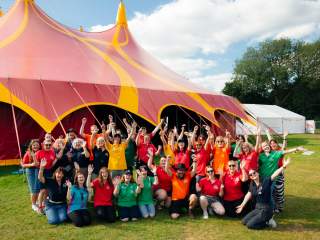 The team from Big Malarkey Festival in colourful t shirts in a group in front of a big red and yellow marquee.