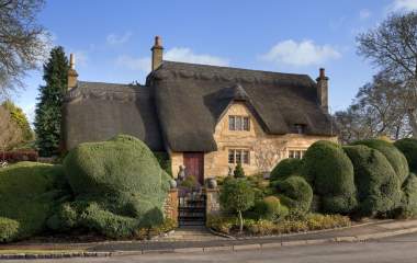 A beautiful thatched cottage surrounded by topiary trees from Manor Cottages in the Cotswolds