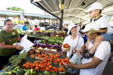 Family buying produce from a woman st the Ann Arbor Farmers Market