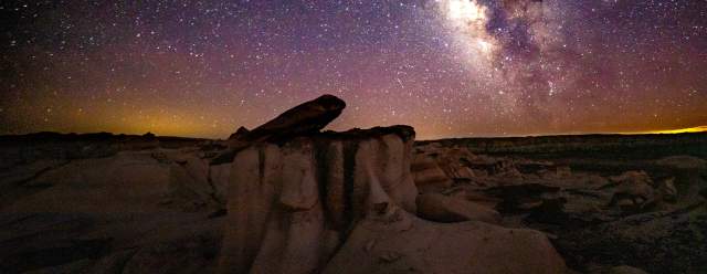 shadowed rock formations span far into the distance, beneath a bright constellation of stars spanning the entire sky