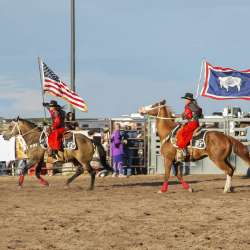 Two horse back riders post the colors at a rodeo