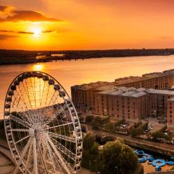 A drone view above the Liverpool Wheel ferris wheel, the Royal Albert Dock buildings and acoss the river as the sun is setting behind the Wirral.