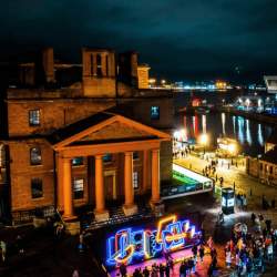 Part of the royal albert dock at night with a light installation on the front.