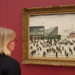 A person standing looking at the famous L S Lowry painting, Going To The Match.