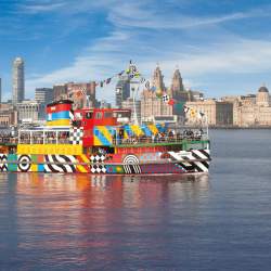 The Mersey Ferry painted in different colours on the river mersey with the skyline in the background