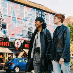 Two people stand on Victoria Road next to a venue called 'Rockpoint Records' that has pink and blue street art