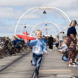 A young boy running along the Southport Traditional Pier. They are holding a blow up aeroplane