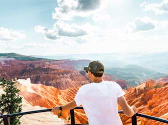 Person standing at scenic overlook at Cedar Breaks National Monument with a red rock canyon in the background and blue skies.