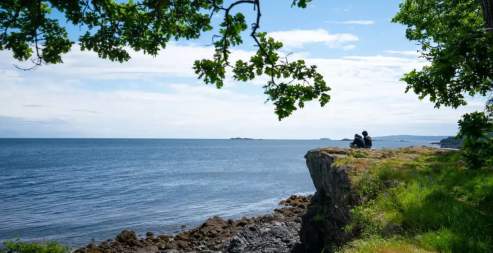 Two people sitting on a cliff looking over the ocean.