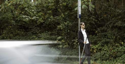 A blind man waiting at a bus stop.