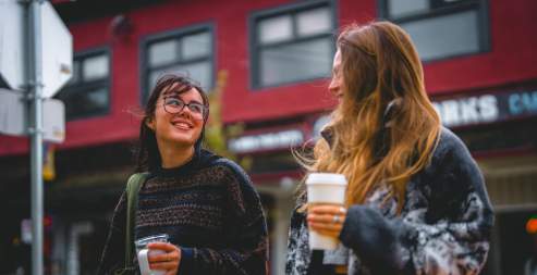 Two people walking holding coffees and chatting.