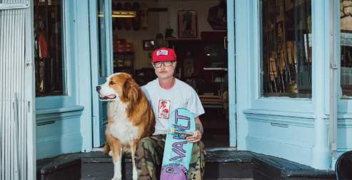 Aa man and his dog sitting with a skateboard.