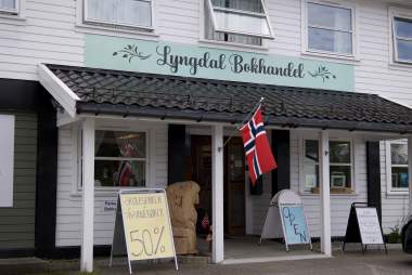 Inngangspartiet til Lyngdal Bokhandel med norsk flagg og tilbudsskilt.
