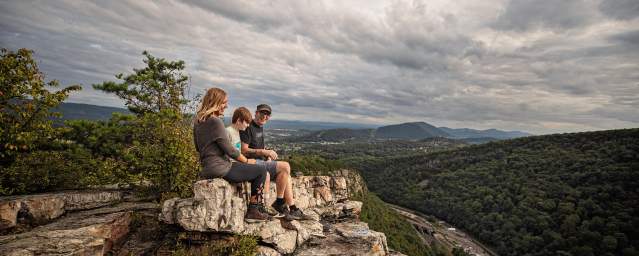 A mom, dad and son sit on a shale cliff overlooking a mountain vista.