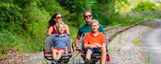 Family of four enjoying the Tracks and Yaks rail biking and kayaking adventure in Allegany County, Maryland, on a sunny summer day.