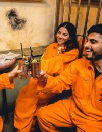 Group with cocktails wearing orange jumpsuits in a cell - credit Alcotraz