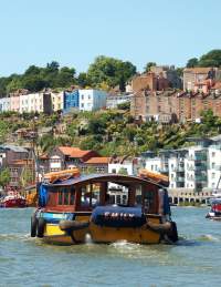 A Bristol Ferry Boat sailing eastwards on Bristol's Harbourside, with the SS Great Britain and colourful houses of Cliftonwood in the background - credit Visit West