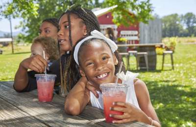 A girl at a picnic table smiles with her pink lemonade.