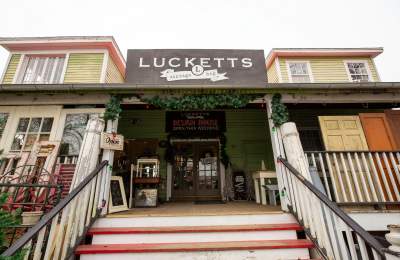 Exterior of Old Lucketts Antique Store with a green and red exterior. The entrance has festive greenery and various antiques displayed outside.