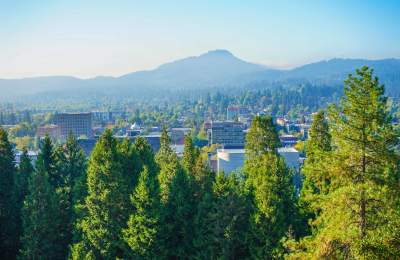 A viewpoint overlooking the city of Eugene shows trees in the foreground, then buildings and streets with a mountain butte in the background.