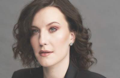 Stephanie Doche wears a black blazer over a red top, posing against a neutral background. The image conveys a professional ambiance.